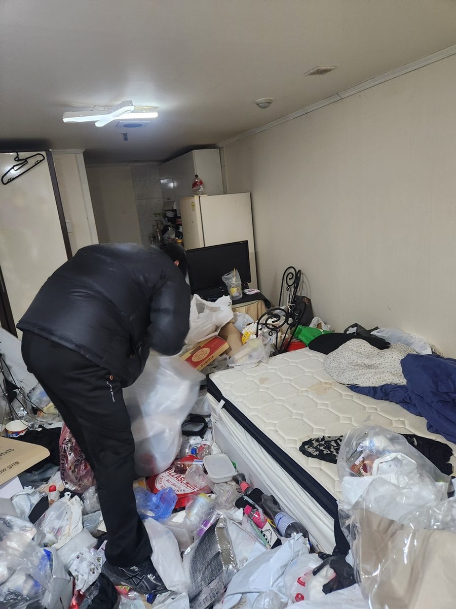 작업자가 원룸 쓰레기 더미 한가운데서 마대에 담는 모습