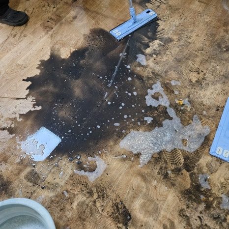 강마루가 걷힌 합판 바닥의 검은 부패 얼룩을 밀대로 닦는 모습
